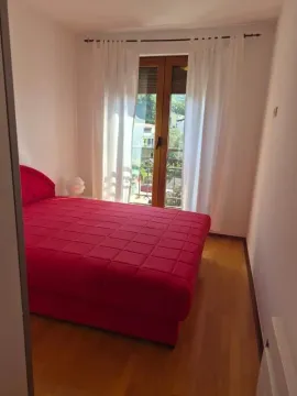 Spavaća soba sa velikim crvenim krevetom i balkonskim vratima. - image 3