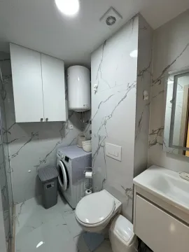 Savremeno opremljeno kupatilo sa bijelim pločicama sa teksturom mramora, veš mašinom i tuš kabinom. - image 7