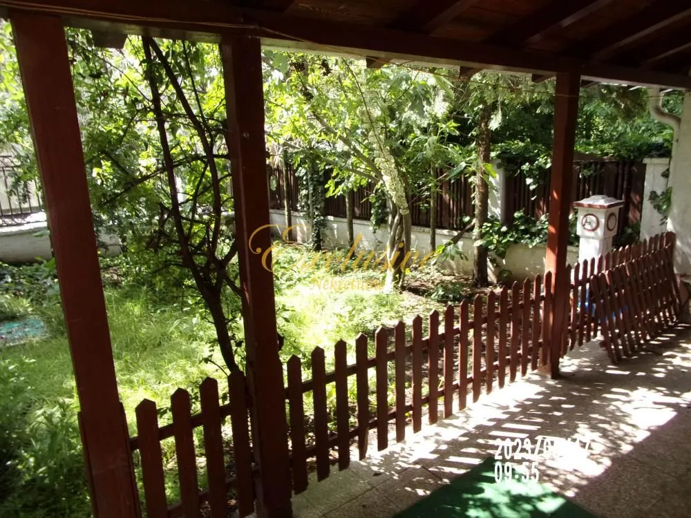 Natkrivena terasa sa drvenom ogradom i pogledom na zeleno dvorište.