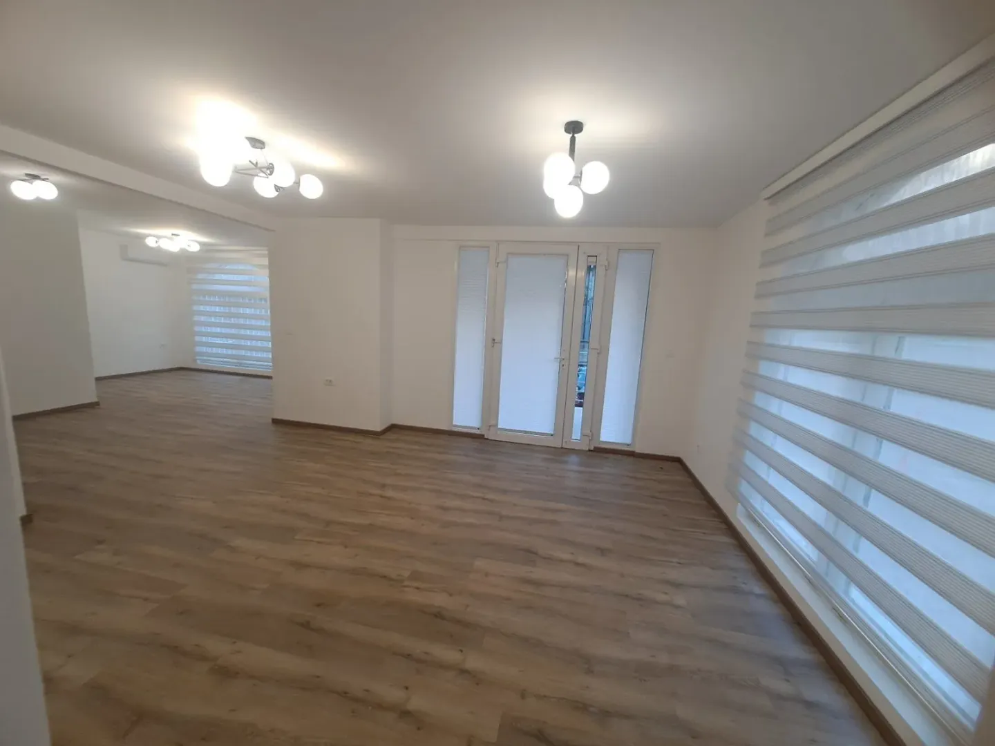Empty spacious living room with wooden flooring and large windows.