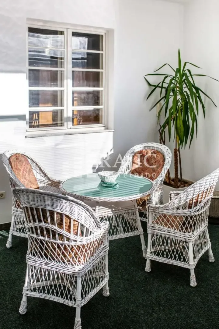 Covered terrace with wicker seating furniture and a decorative plant.