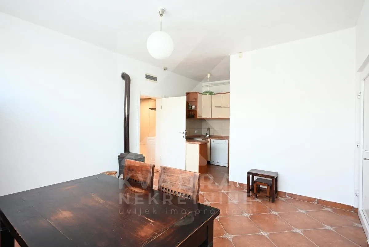 Living room with a dining table and wood stove, looking towards the kitchen in the background.