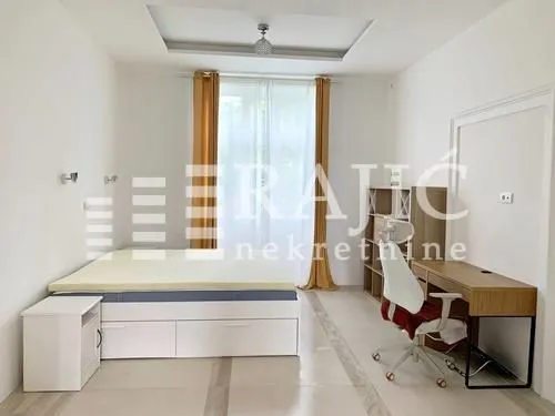 Furnished bedroom with a bed, desk, and white walls.