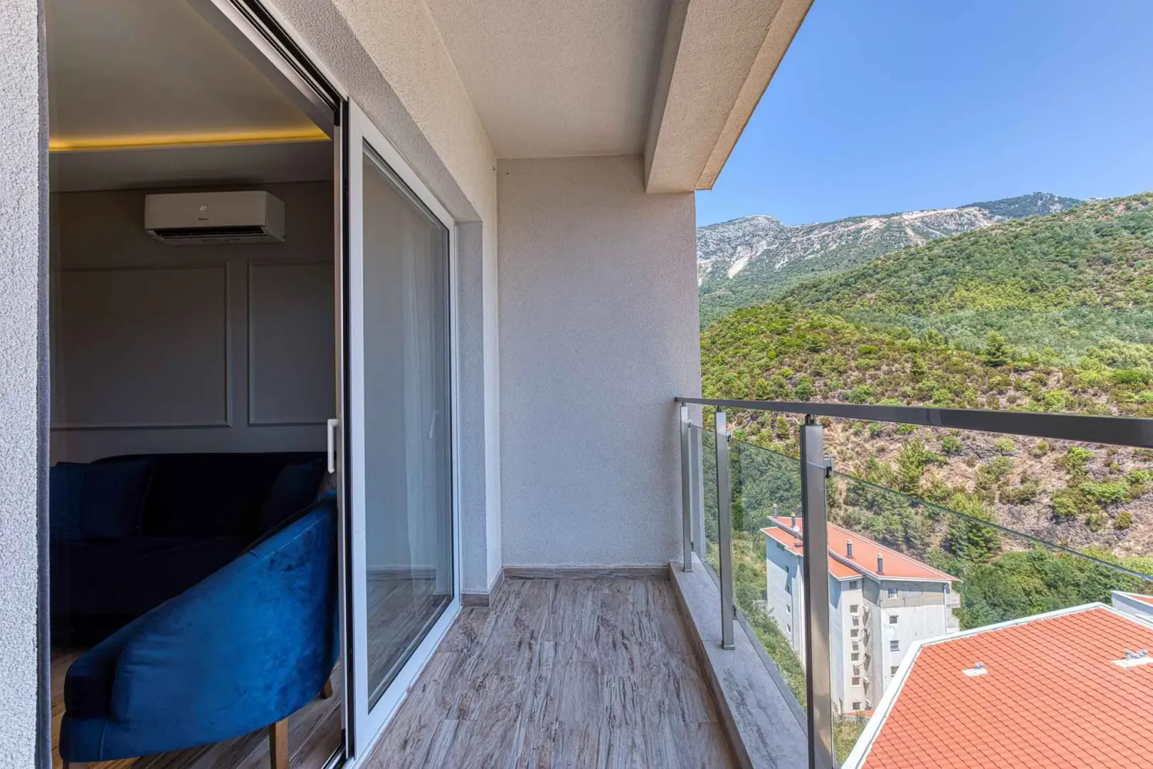 Balkon sa staklenom ogradom i pogledom na prirodu i okolne zgrade.