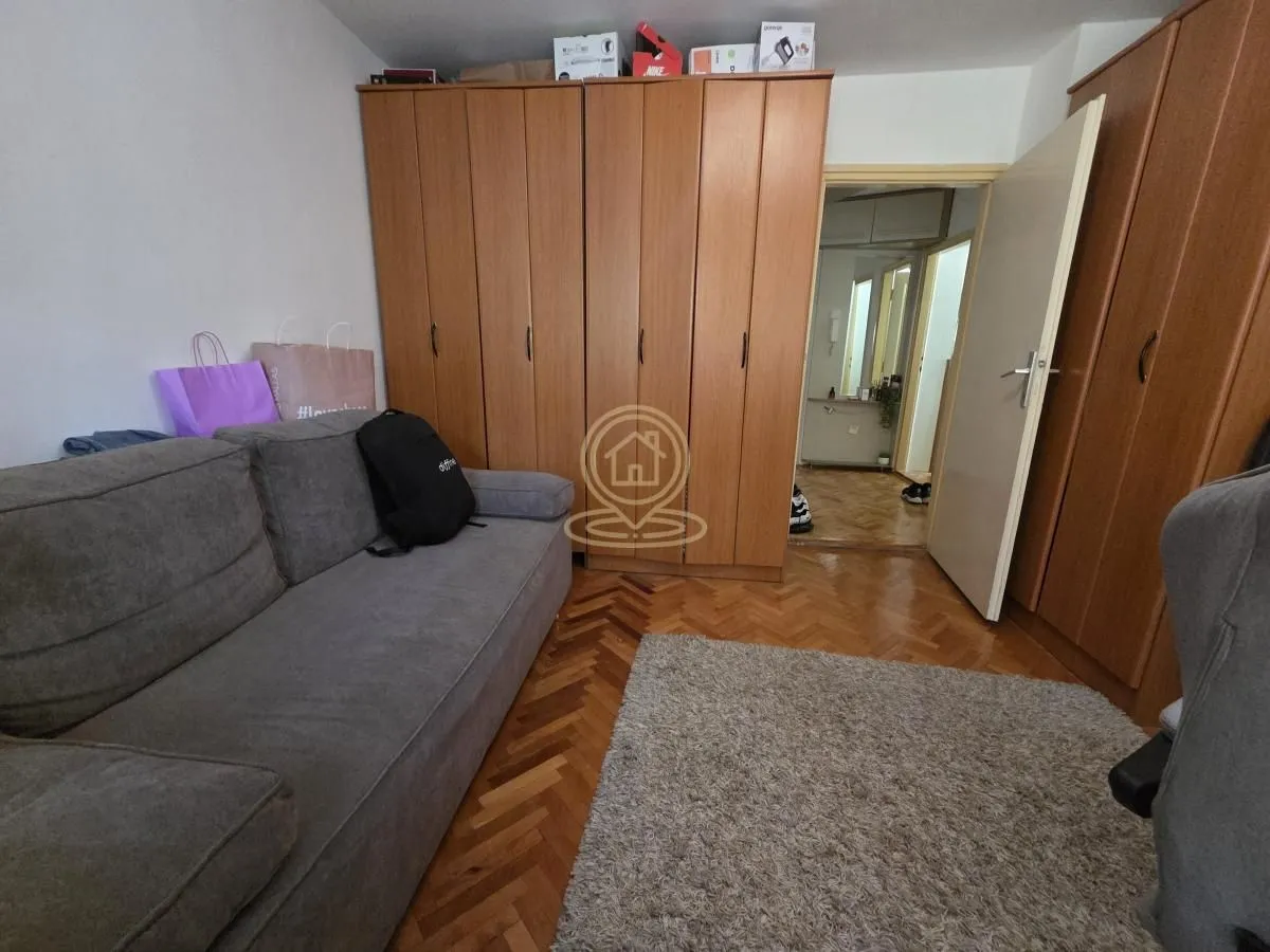 Dnevna soba sa sivom garniturom, drvenim ormarima i parketom na podu.