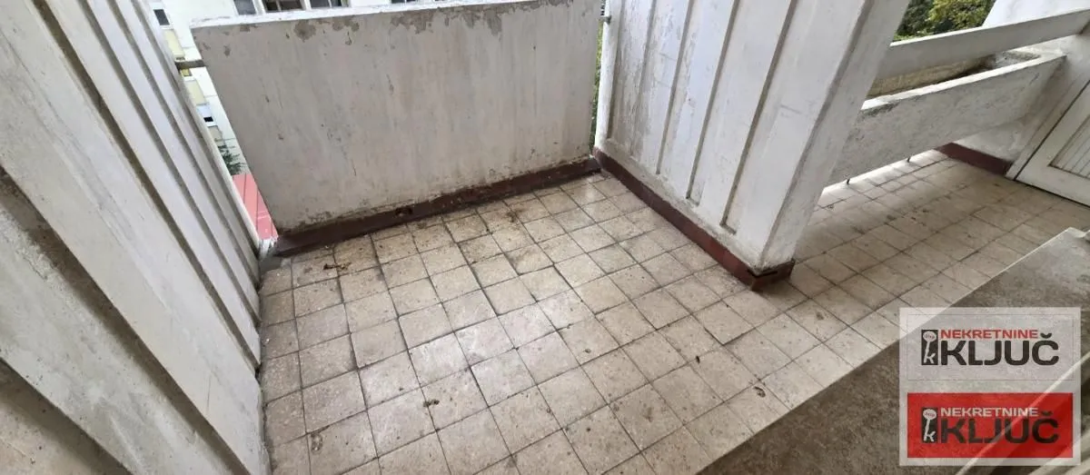 Prazan balkon sa keramičkim pločicama i starom ogradom.