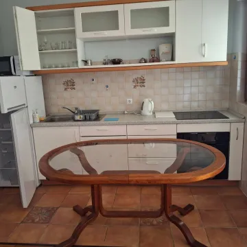 Kuhinja sa bijelim elementima, sudoperom, ugradnom pločom i trpezarijskim stolom u sredini. - image 6