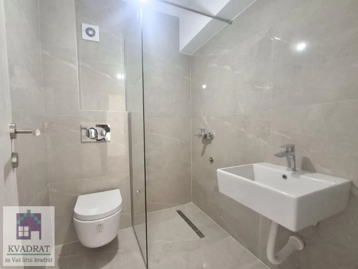 Modern bathroom with a walk-in shower, washbasin, and wall-hung toilet tiled with light-colored tiles.