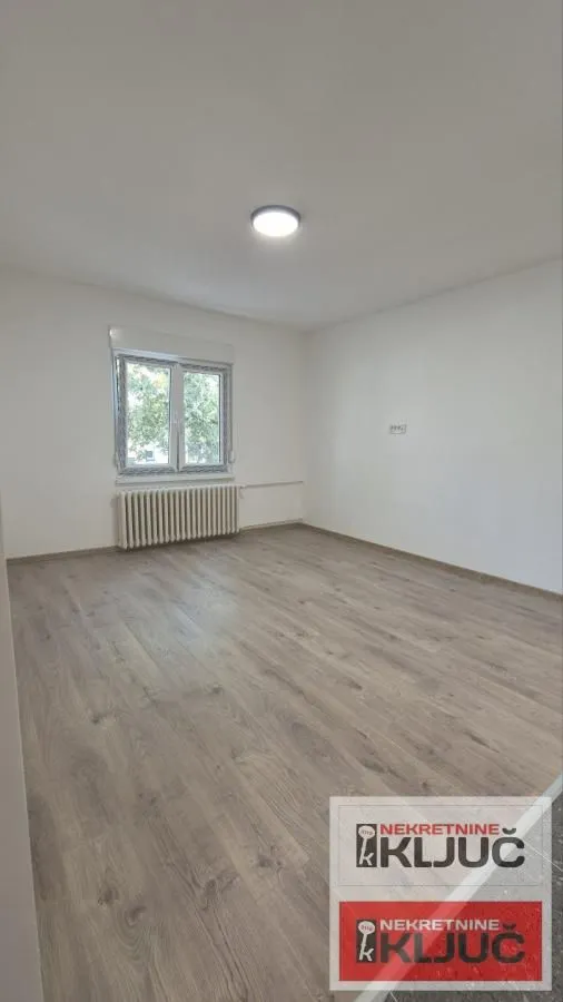 Prazna soba sa laminatom i jednim prozorom.