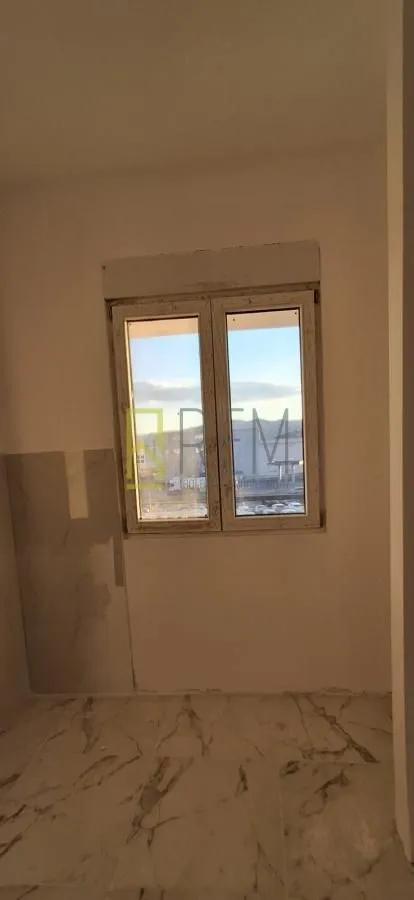 Prazna prostorija sa prozorom i svijetlim keramičkim pločicama na podu.