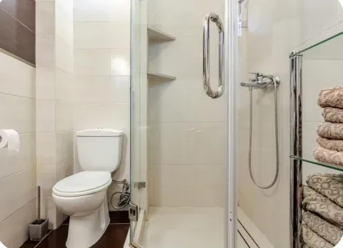 Bathroom equipped with a shower cabin, toilet, and shelves with towels. - image 4