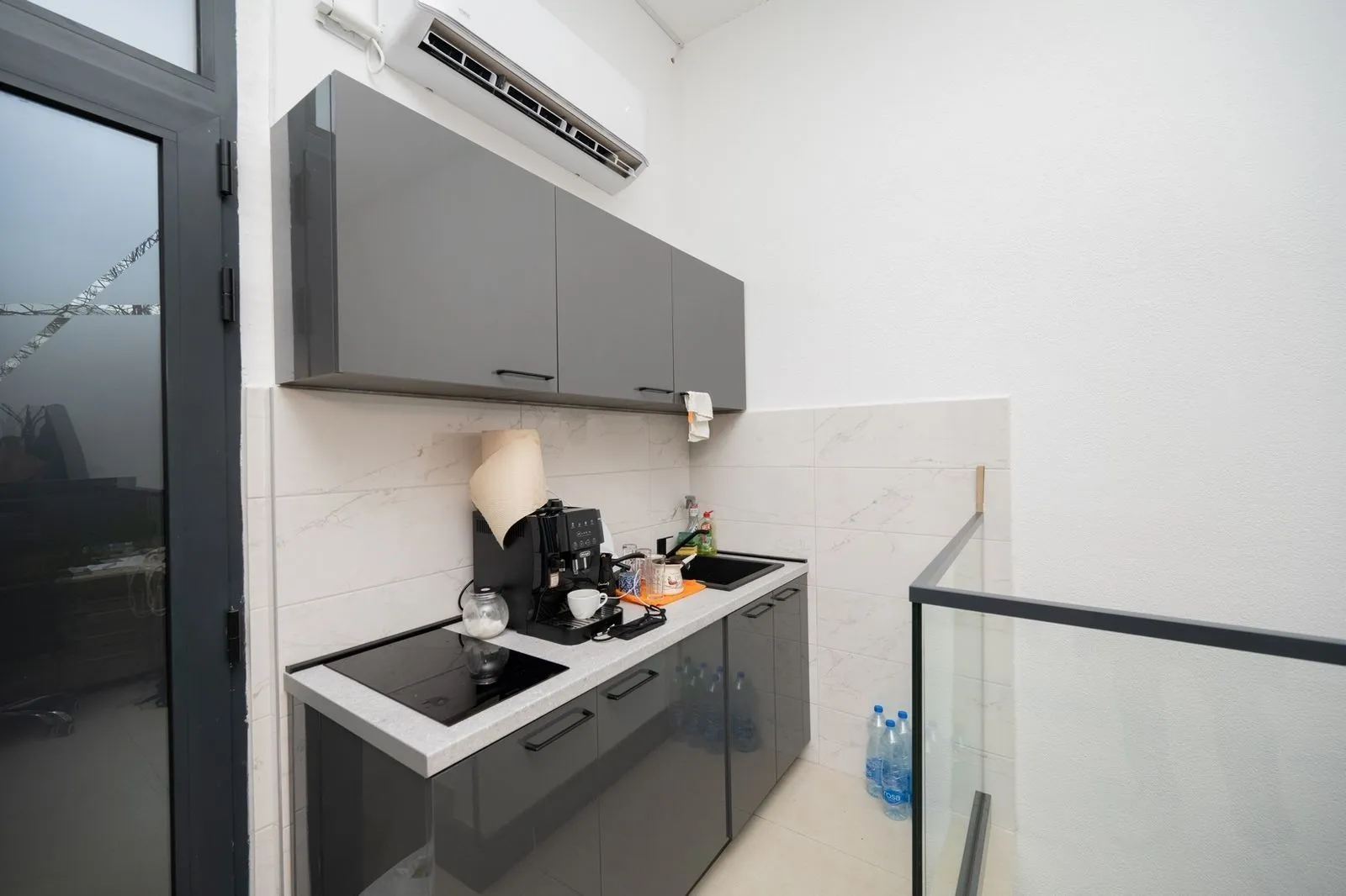 A small functional kitchen with grey cabinets and an air conditioner.