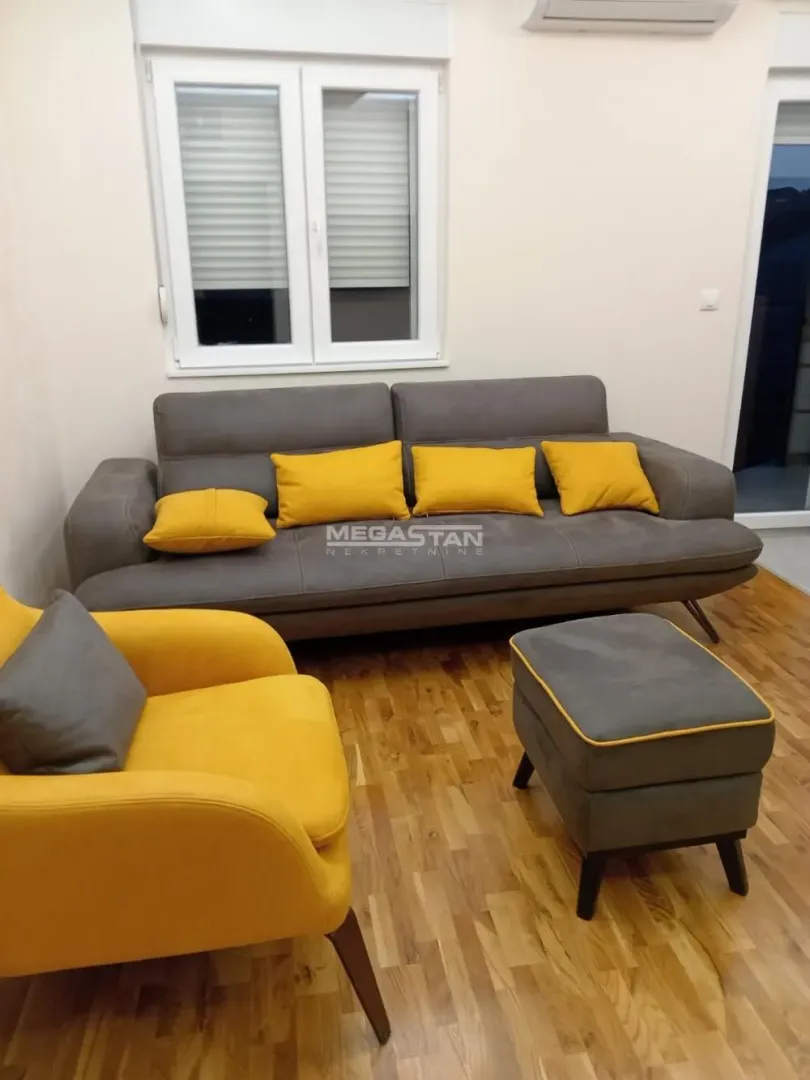 Dnevna soba sa sivom garniturom, žutim jastucima i foteljom.