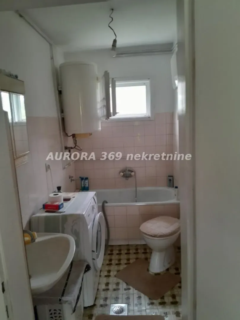 Manje kupatilo sa kadom, umivaonikom, veš mašinom i WC šoljom.