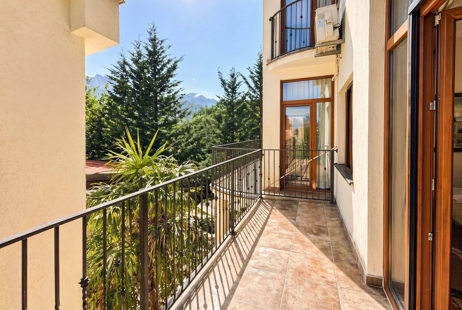 Spacious balcony with metal railing and view of greenery and mountains.