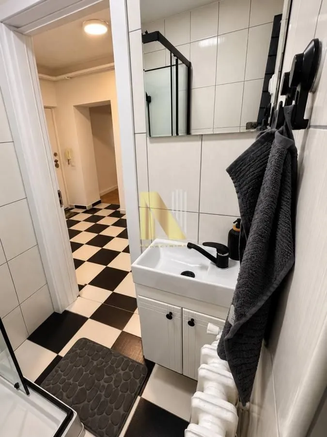 Manje kupatilo sa belim pločicama, umivaonikom i crnim detaljima.