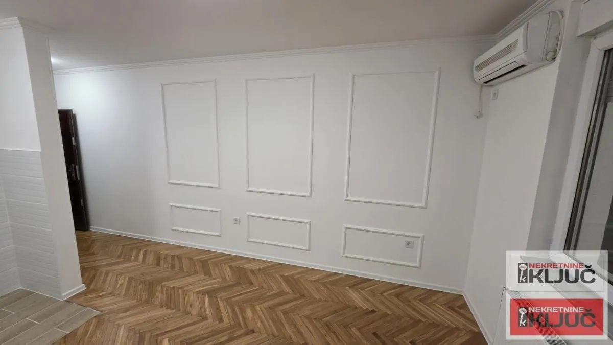 Prazna soba sa drvenim parketom i ukrasnim lajsnama na zidu.