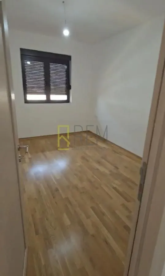Prazna soba sa parketom i prozorom sa roletnama.