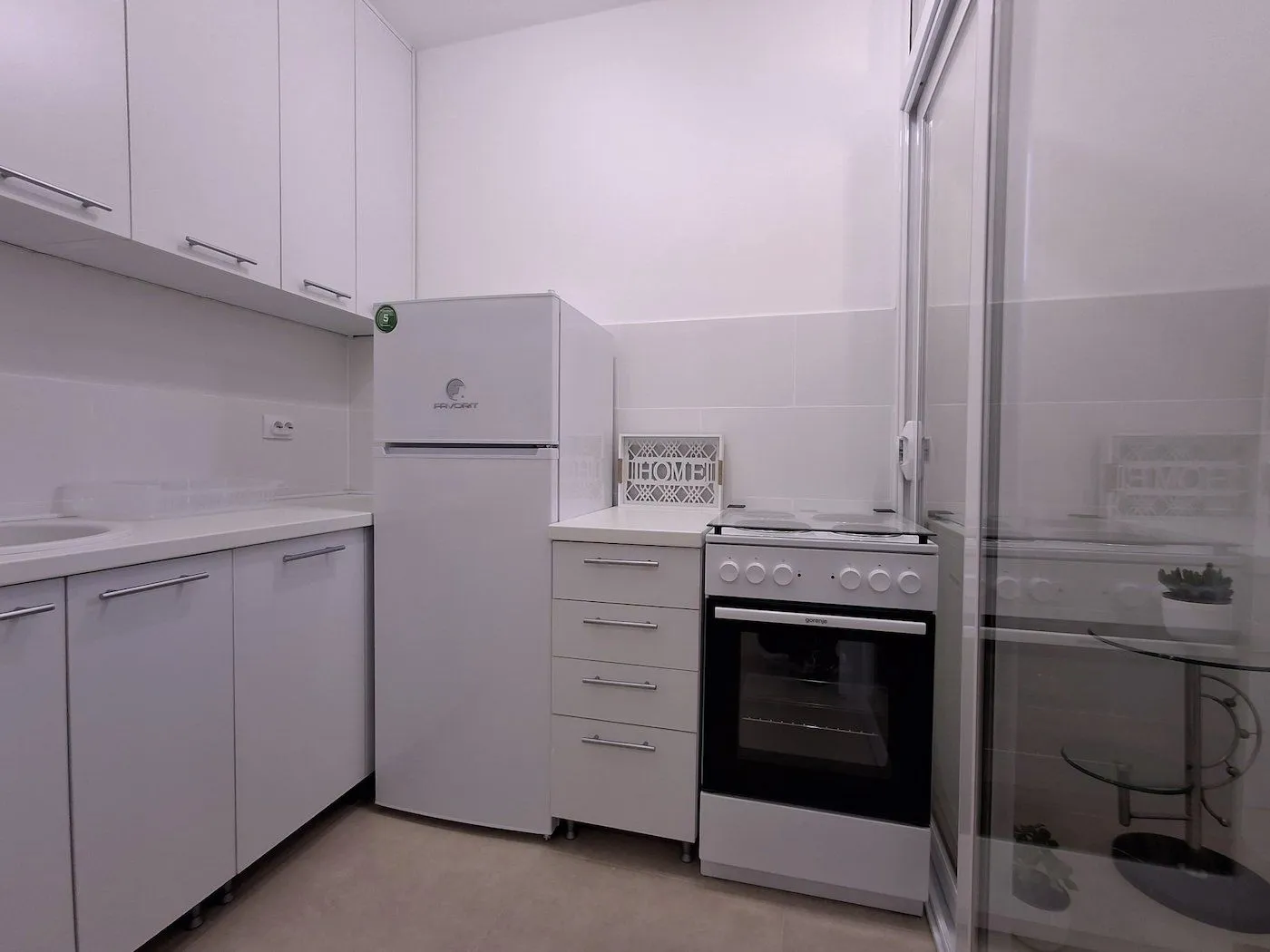 Manja bijela kuhinja sa frižiderom i šporetom.