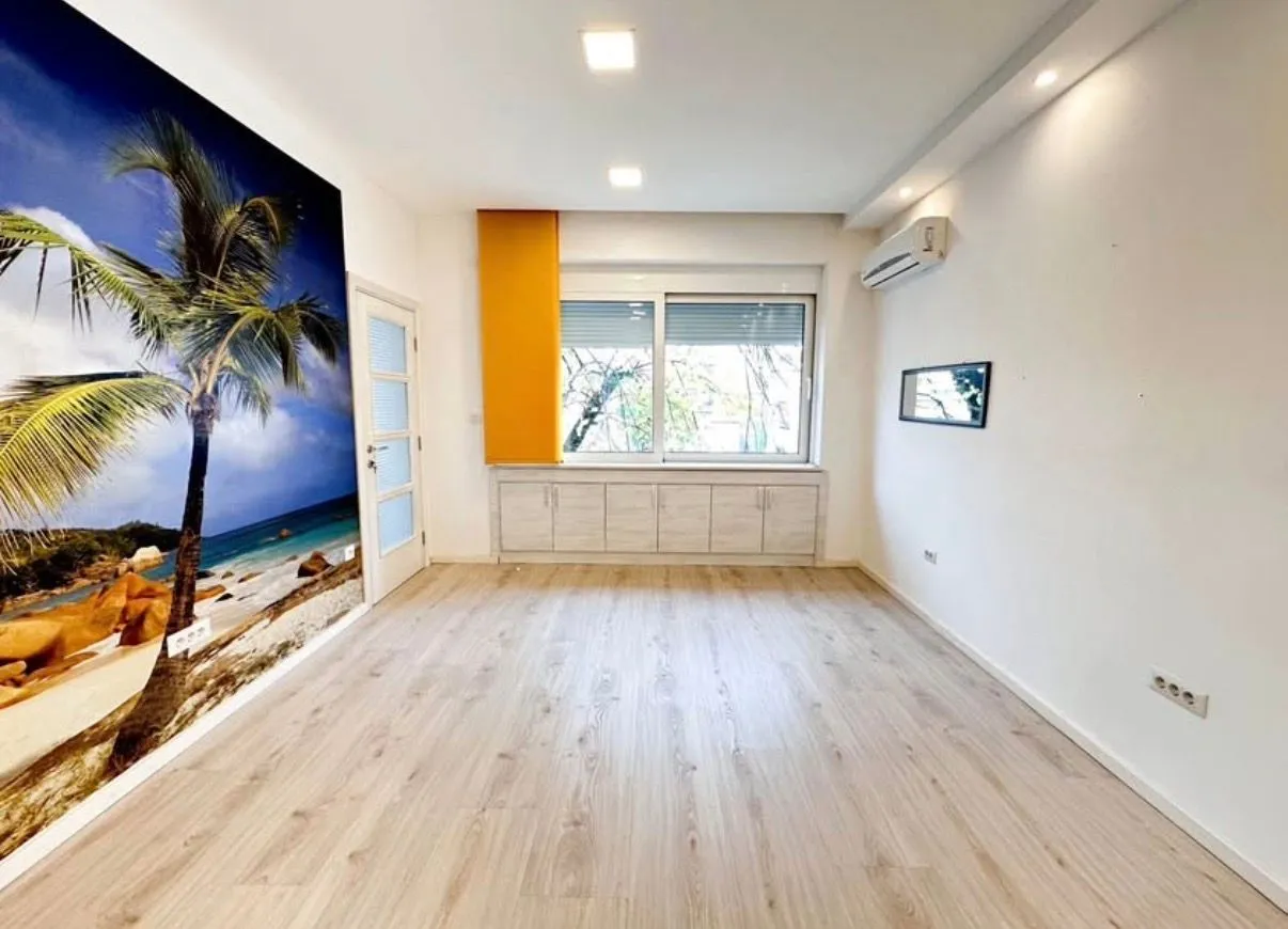 Empty room with laminate flooring and a beach motif wallpaper on the wall.