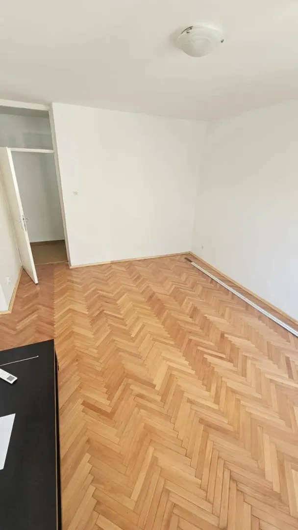 Prazna soba sa parketom i bijelim zidovima.