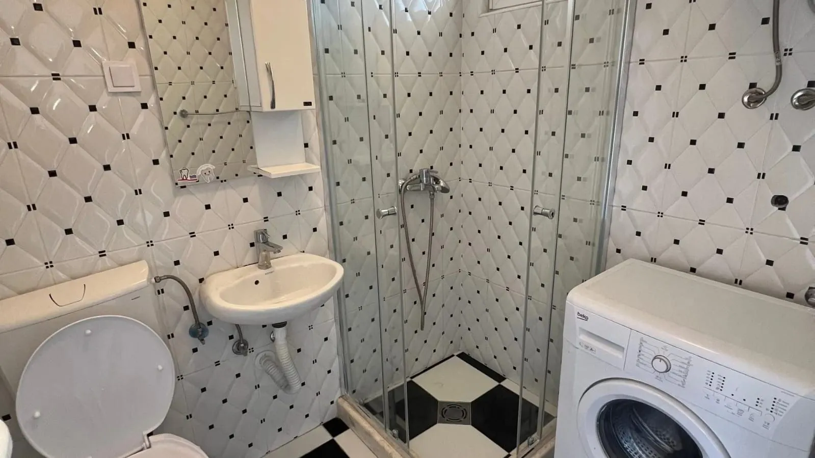 Smaller bathroom with a shower cabin, washbasin, and washing machine.