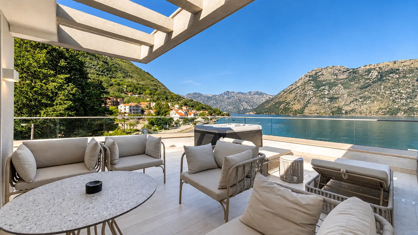 Spacious terrace with seating furniture, a jacuzzi, and a view of the sea and mountains.