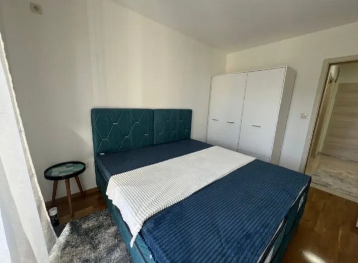 Namještena spavaća soba sa bračnim krevetom, bijelim ormarom i noćnim stočićem.