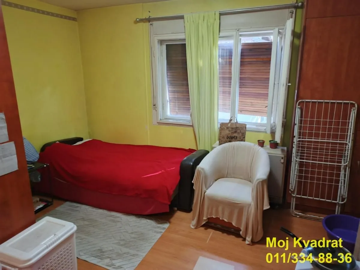 Manja spavaća soba sa krevetom, foteljom i prozorom.