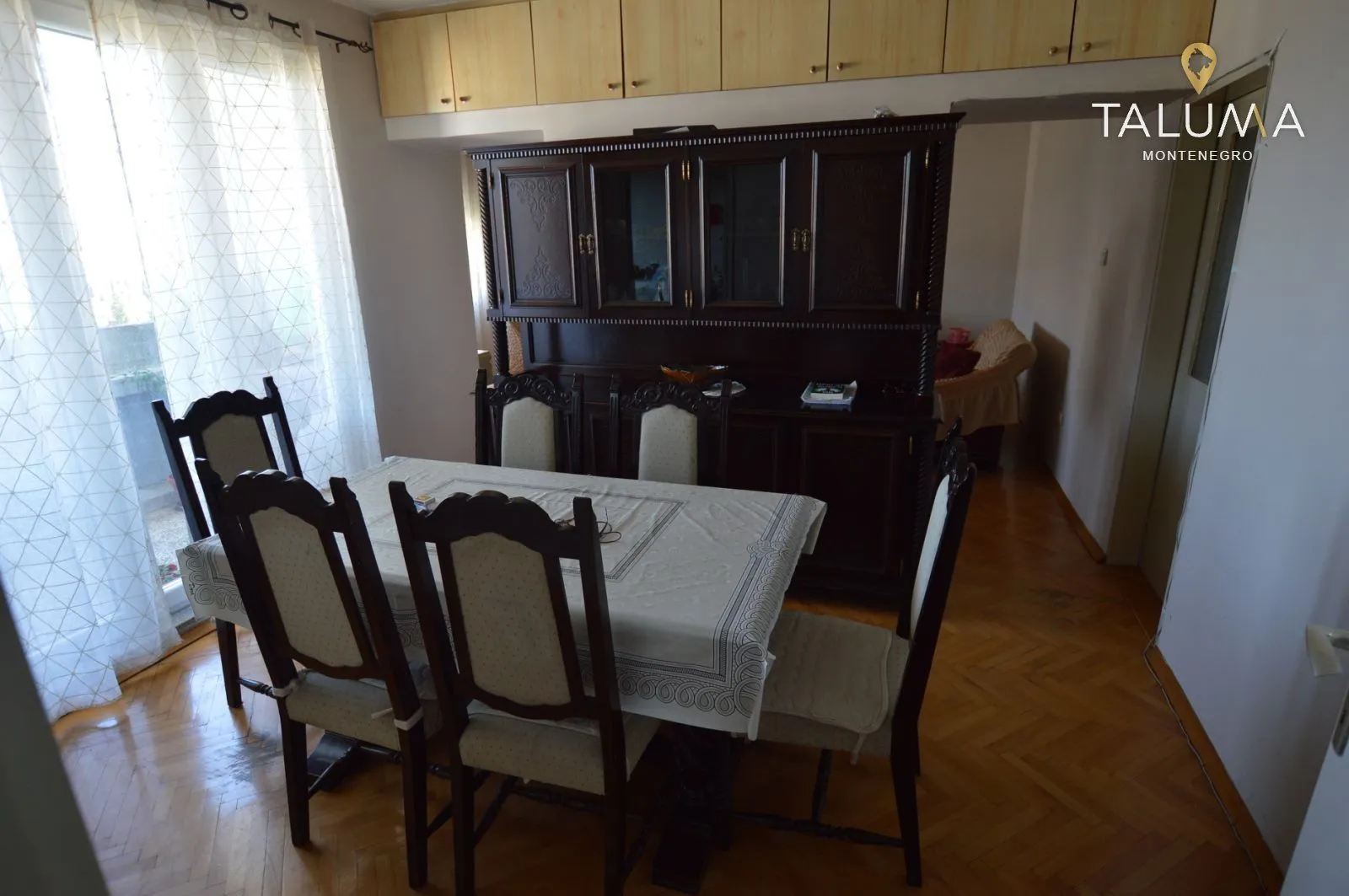 Trpezarija sa drvenim stolom, stolicama i velikim kredencem.