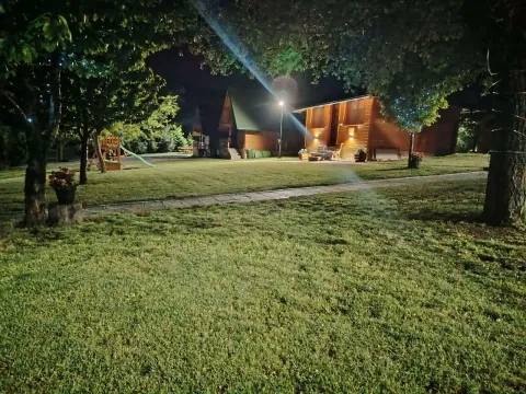 Noćni pogled na osvetljeno dvorište i drvenu kuću sa uređenim travnjakom. - image 5