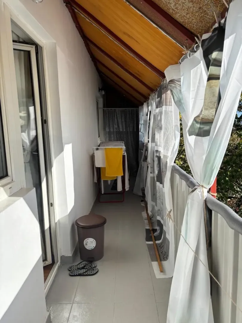 Dugi natkriveni balkon sa sušilicom za veš i zavesama duž ograde.