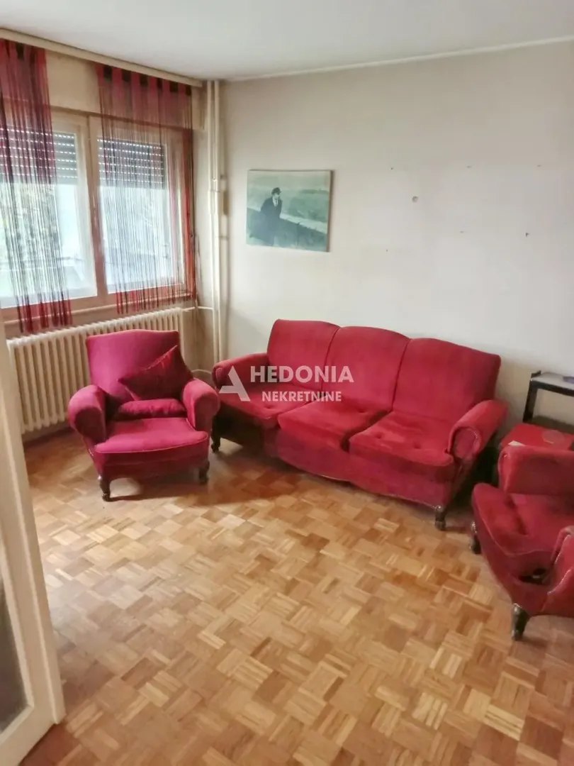 Dnevna soba sa crvenom garniturom i parketom na podu.
