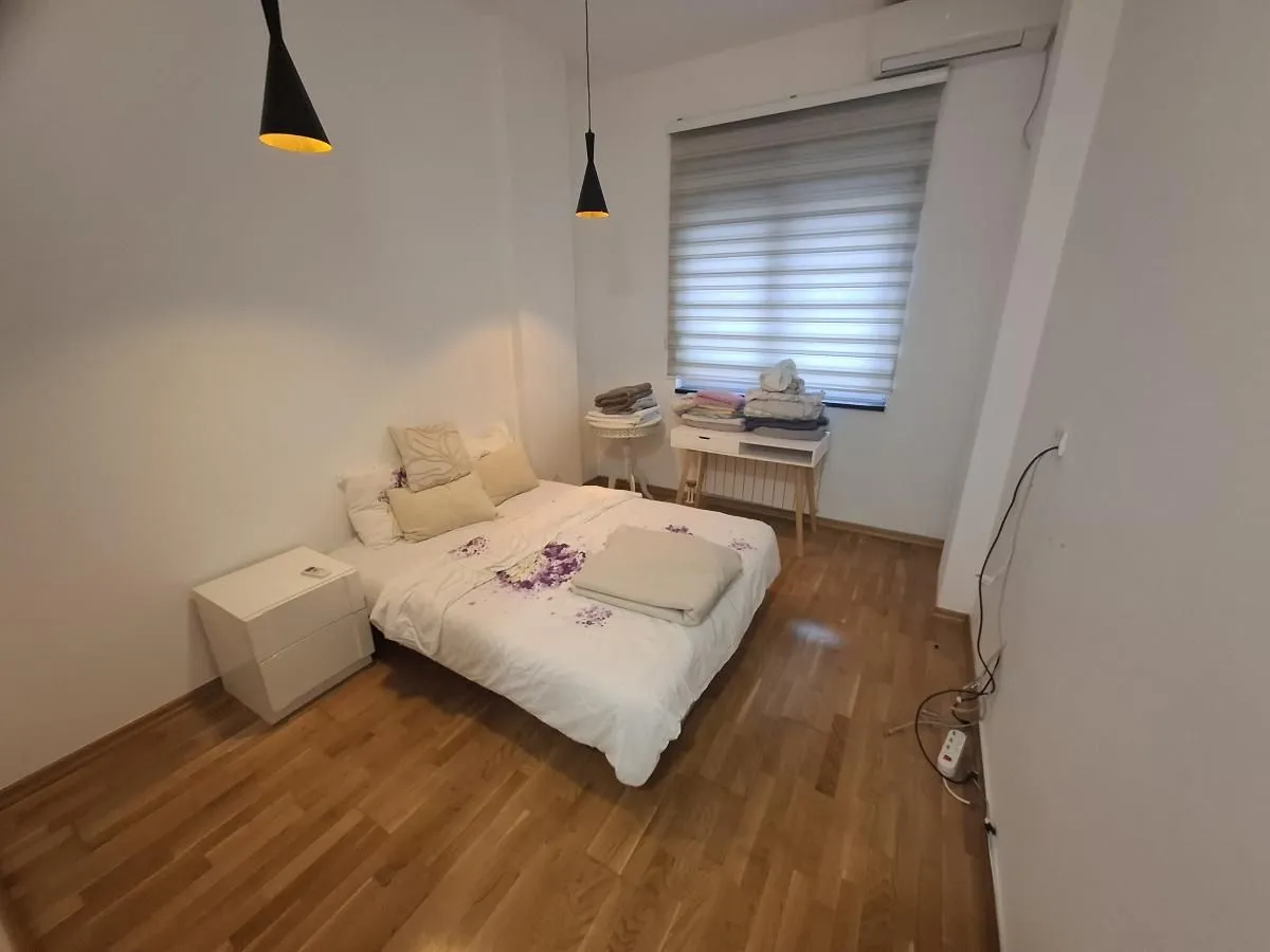 Spavaća soba sa bračnim krevetom, noćnim stočićem i drvenim podom.