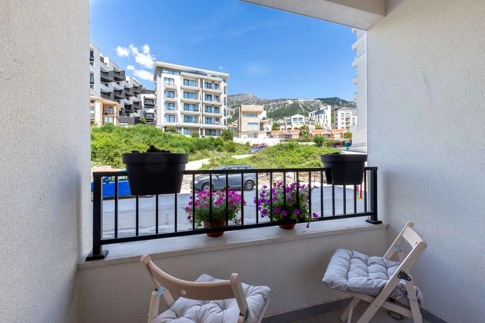 Manji namješteni balkon sa stolicama i pogledom na okolne zgrade i brda.
