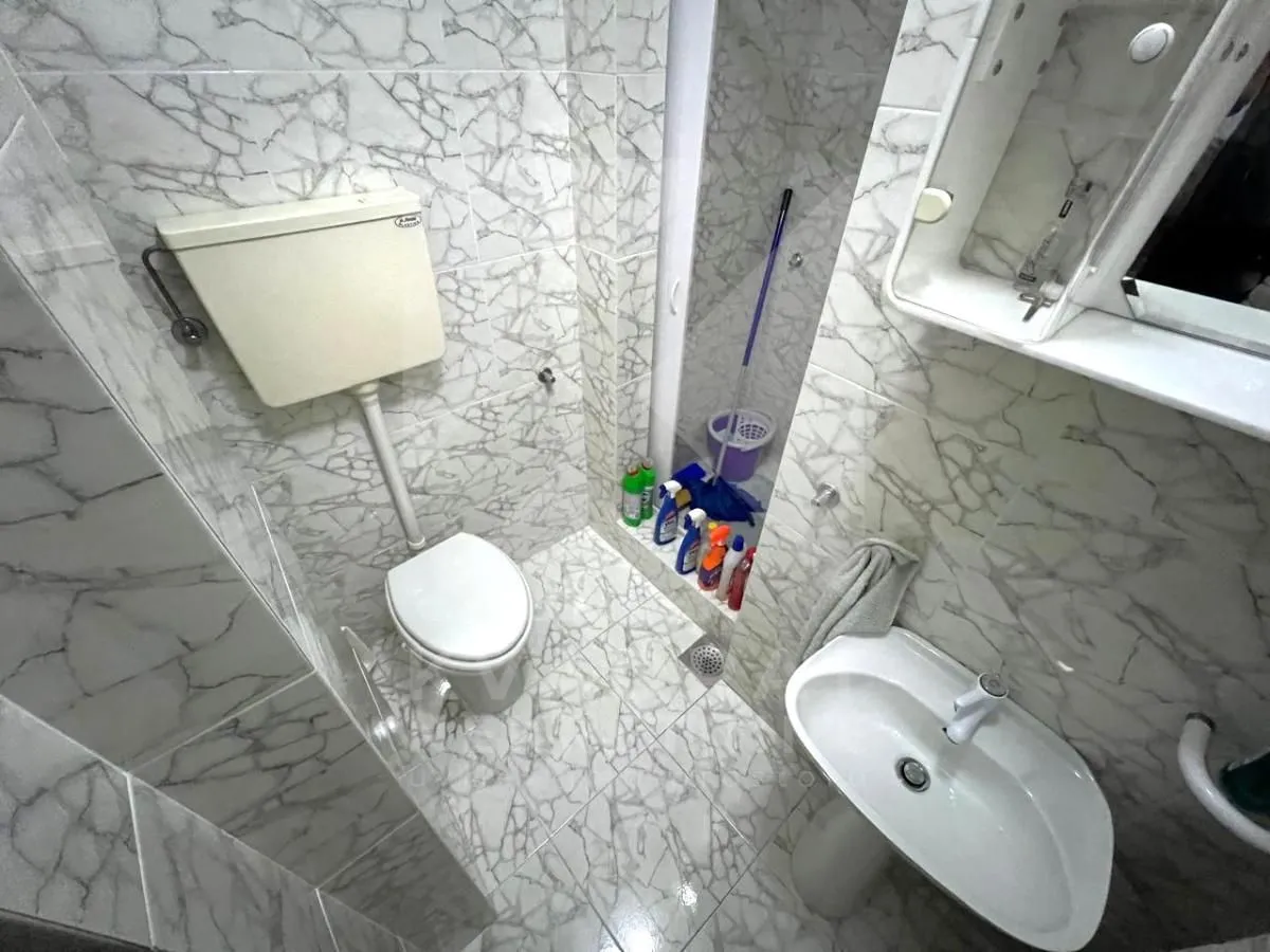 Manje kupatilo obloženo mermernim pločicama sa WC šoljom, umivaonikom i tuš kabinom.