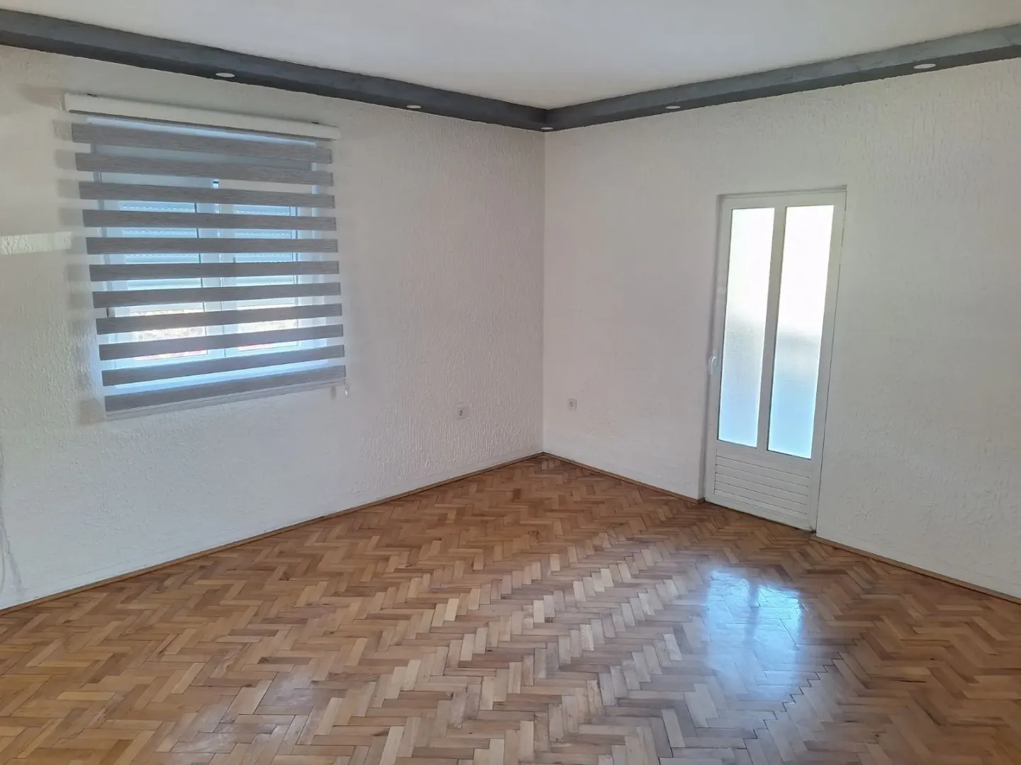 An empty room with parquet flooring and a window with modern blinds.
