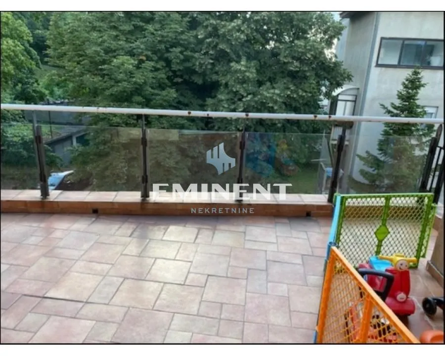 Spacious tiled terrace with a railing and a view of greenery.