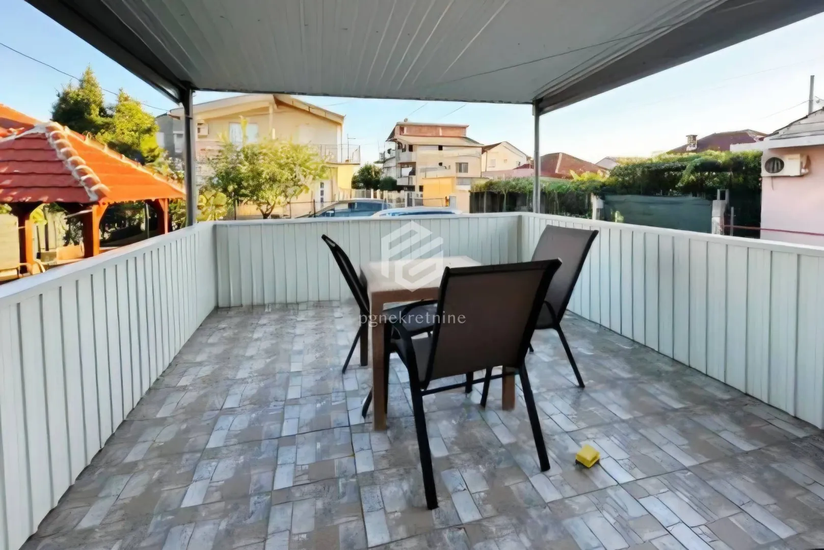 Covered terrace with a table and chairs and a view of the surroundings.