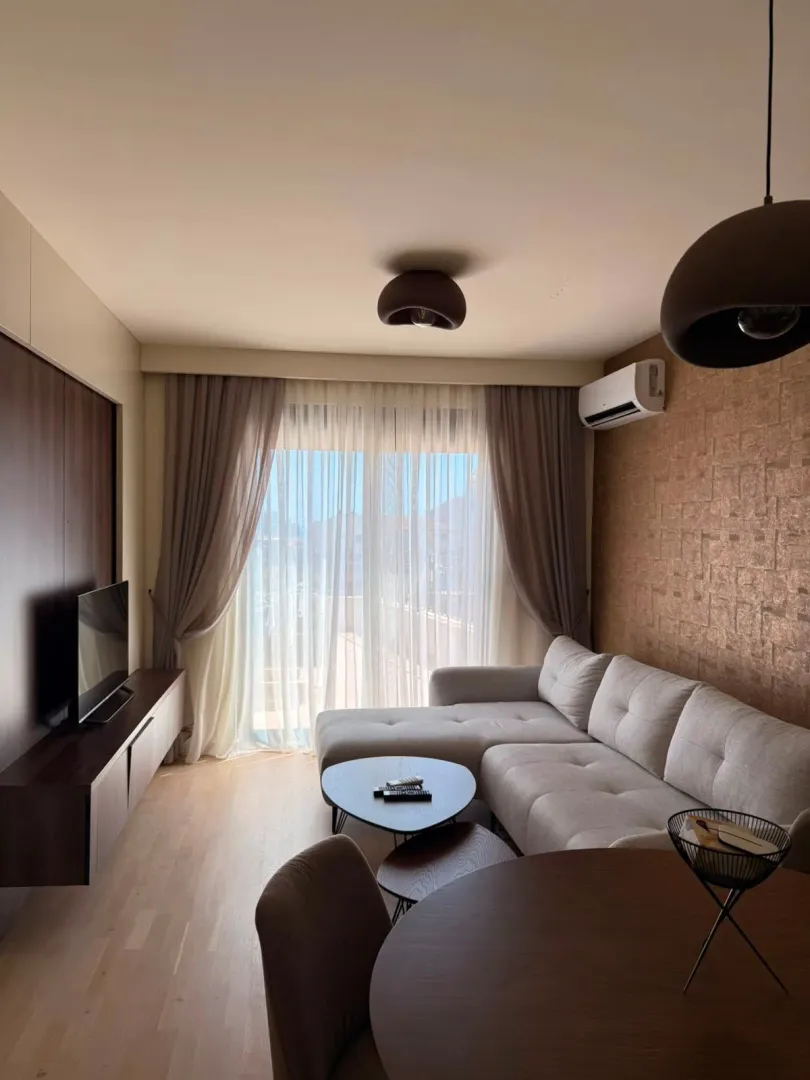 Living room with a sectional sofa, TV unit, and dining table.