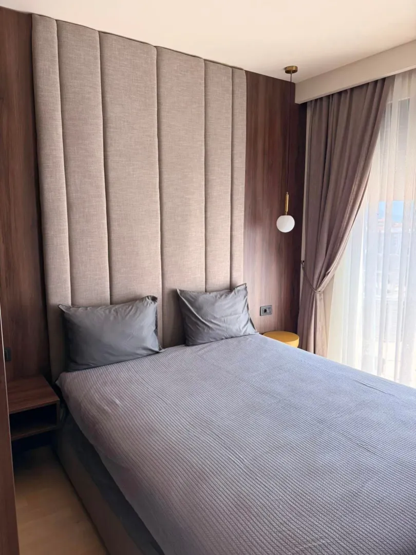 Modern bedroom with a double bed, upholstered headboard, and wooden wall panels.