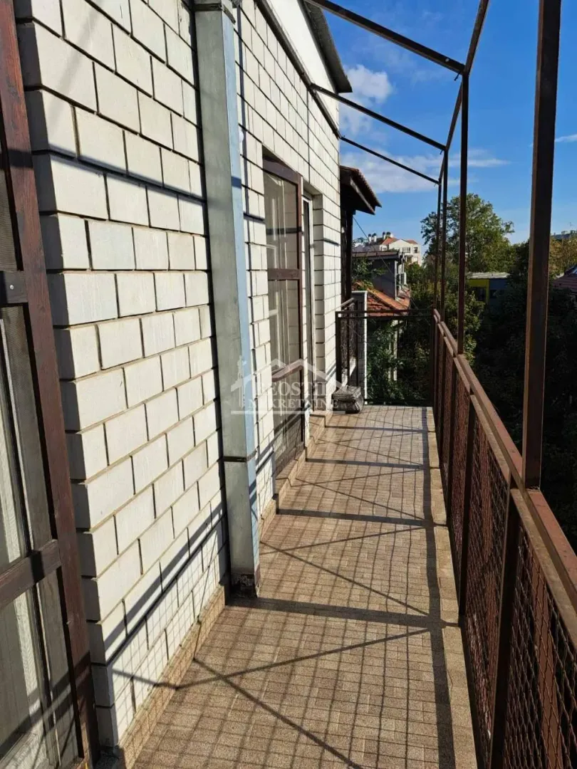 Dugačak popločani balkon sa metalnom ogradom i pogledom na okolinu.