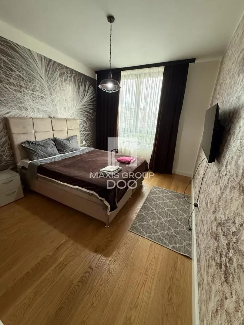 Nameštena spavaća soba sa bračnim krevetom, TV-om i laminatnim podom.