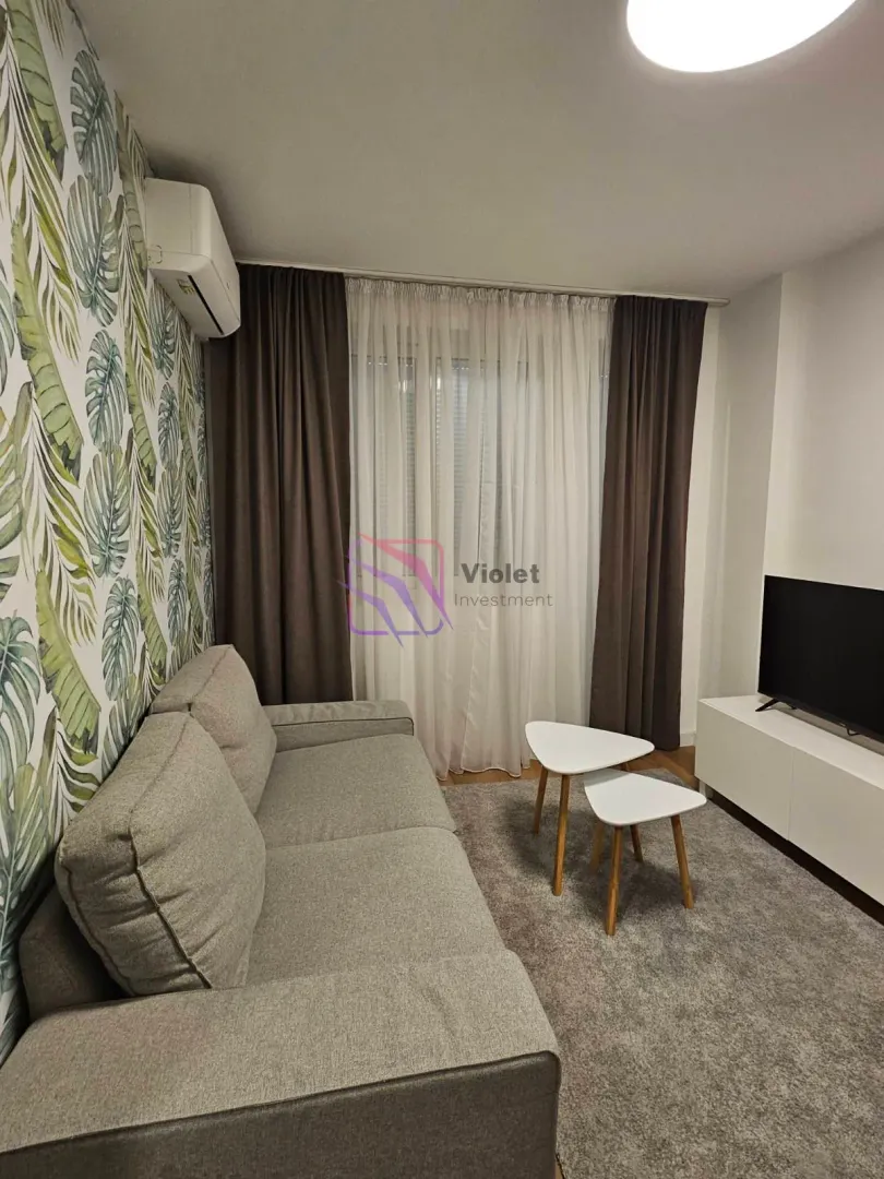 Living room with a grey sofa, TV unit, and botanical-patterned wallpaper.