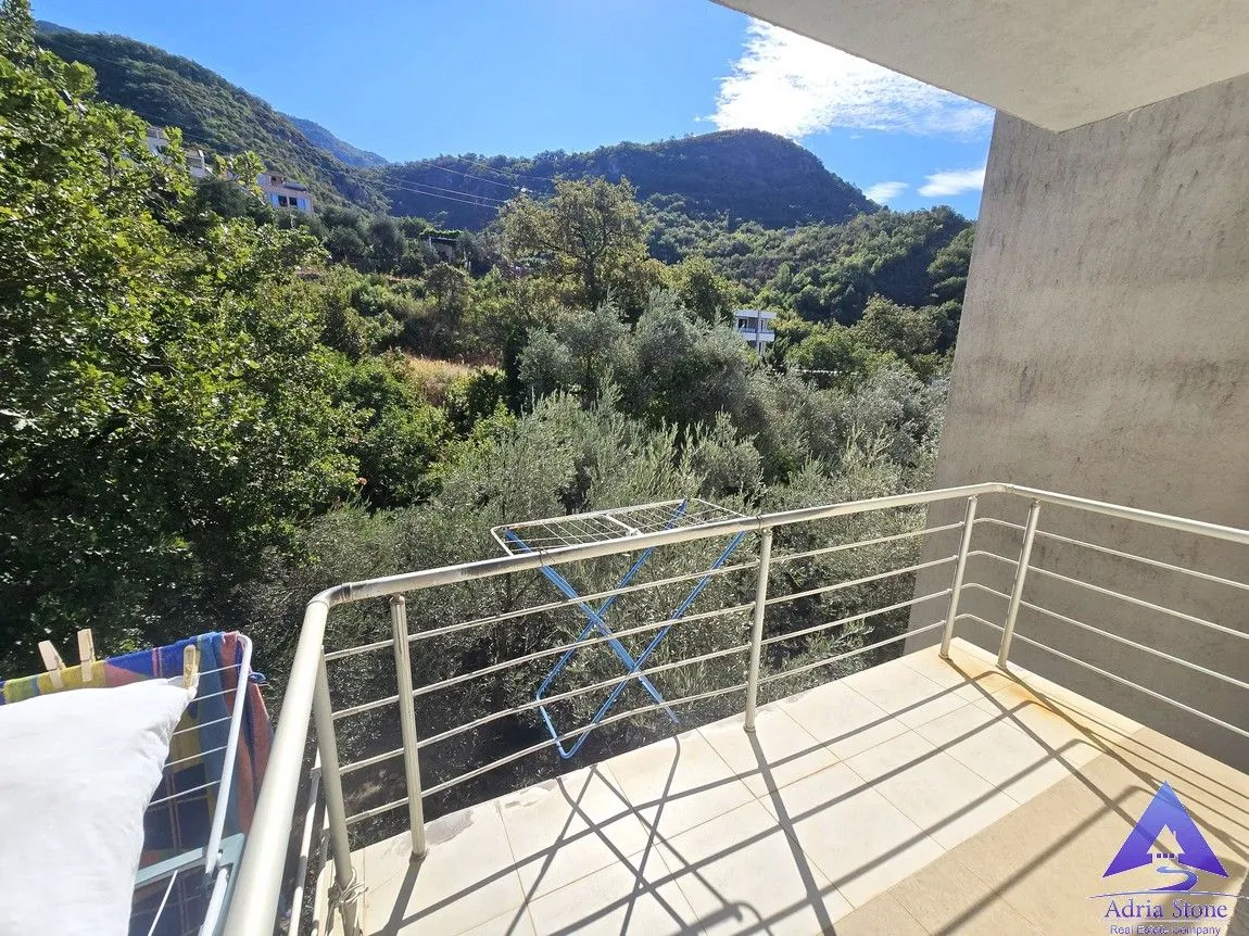 Natkriveni balkon sa metalnom ogradom i pogledom na brda i zelenilo.