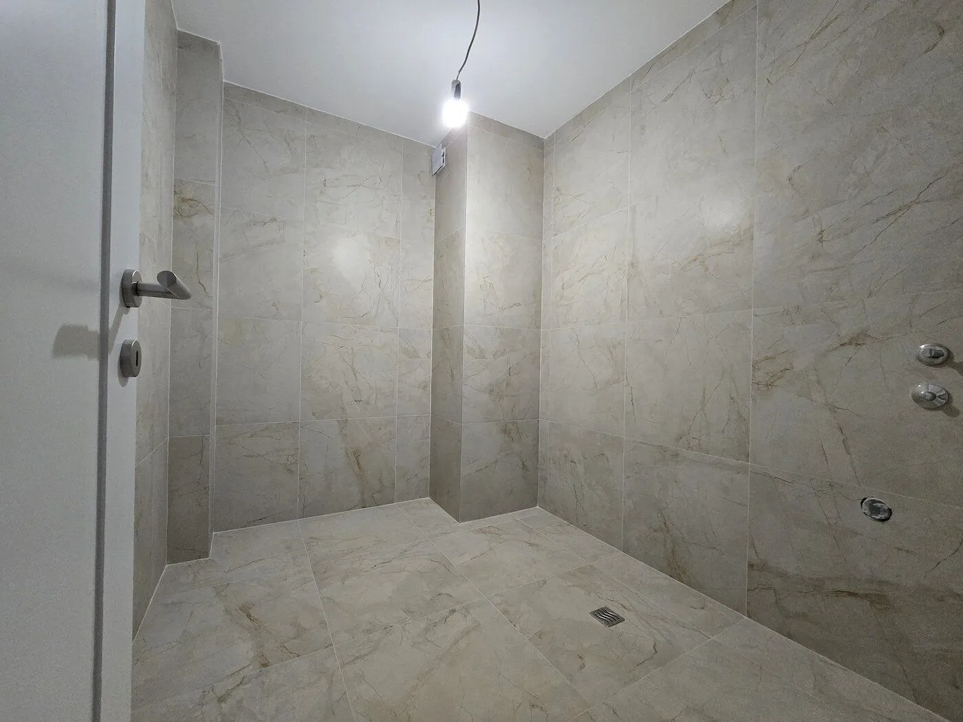 Modern tiled bathroom with a walk-in shower under construction.