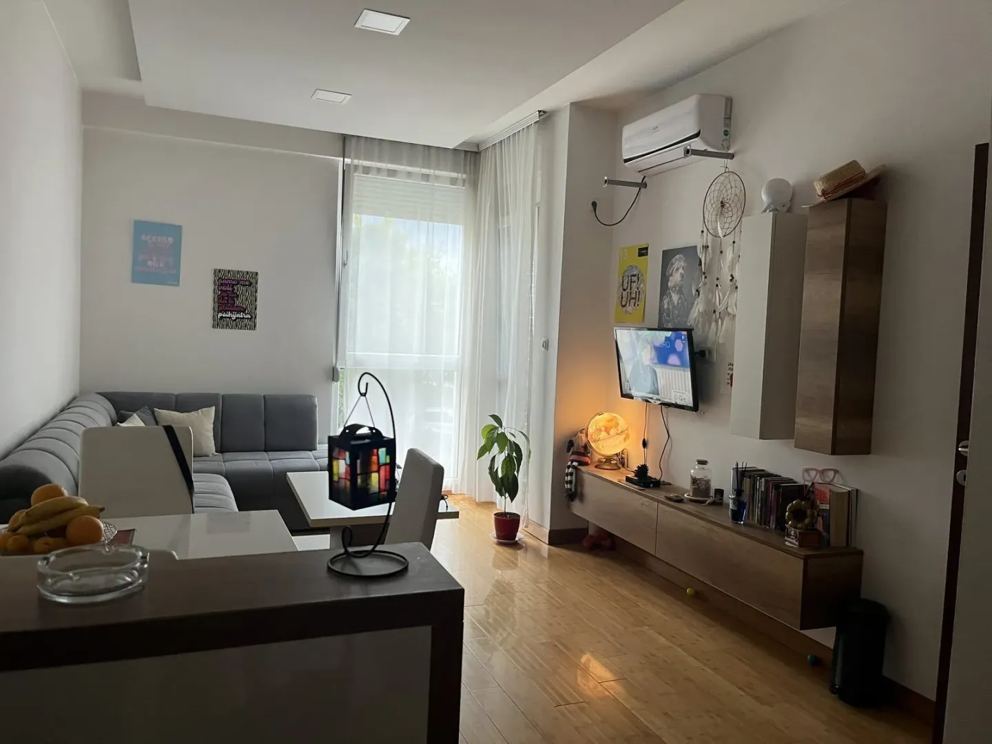 Svijetla dnevna soba sa ugaonom garniturom, televizorom i ukrasnim detaljima.