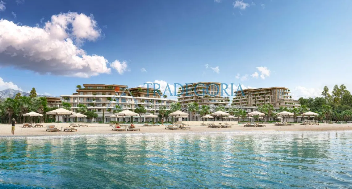 Prikaz eksterijera kompleksa sa plažom i ležaljkama ispred zgrada.