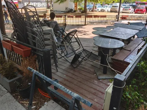 Terrace with a wooden deck, tables, and stacked chairs. - image 6