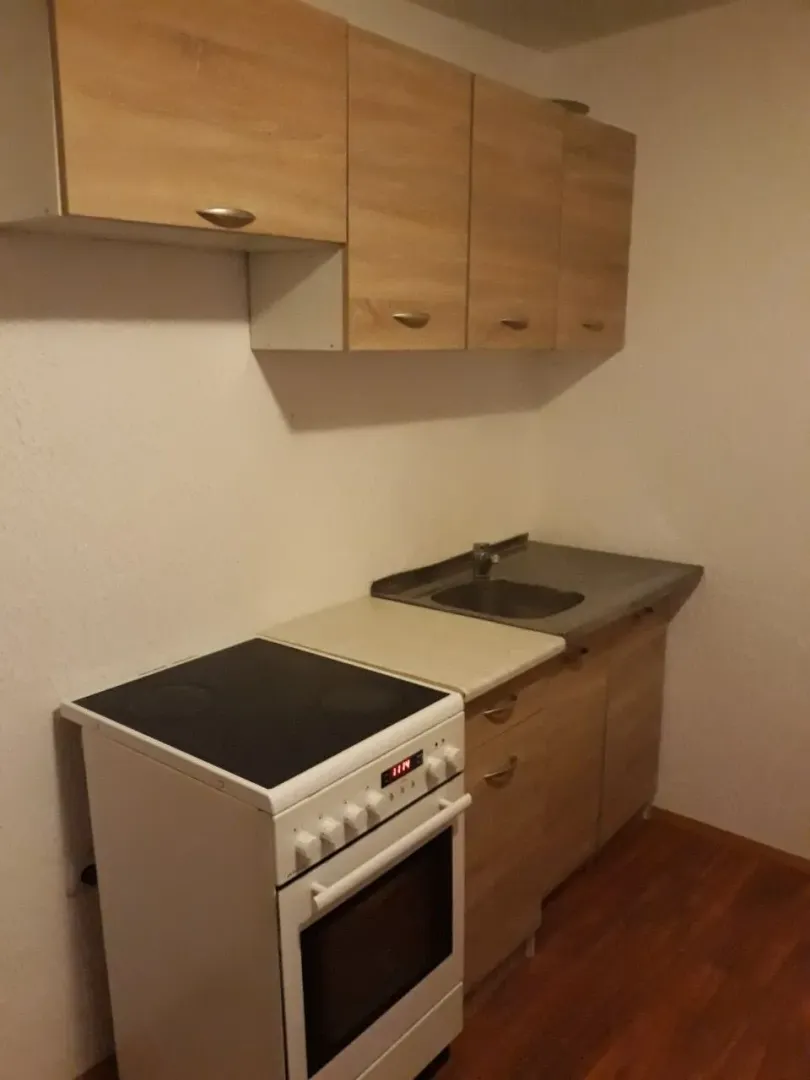 Jednostavna kuhinja sa šporetom i visećim drvenim dijelovima.